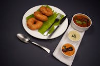 A classic South Indian breakfast featuring vadai served with sambar and chutneys on a black background.
