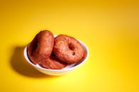 Close-up of traditional Indian vada doughnuts in a bowl on a bright yellow background.
